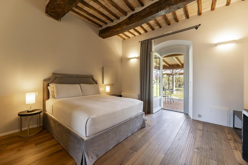 Camera accogliente con letto elegante, soffitto in legno e vista su giardino soleggiato.