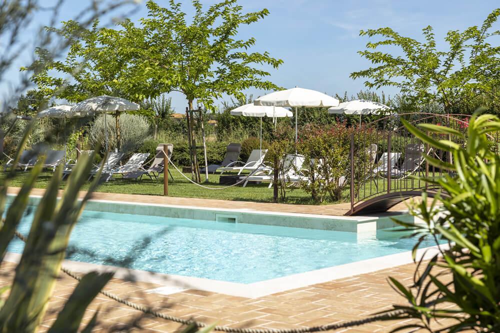 Piscina luminosa, verde rigoglioso, ombrelloni bianchi: un'oasi di relax estivo.